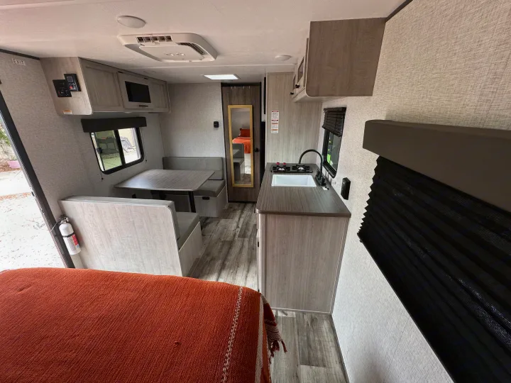 Inside a modern rv rental: kitchen with sink/stove, dinette, and bed with orange blanket. Light wood tones & patterned walls.. Crossroads RV Zinger Lite 2026
