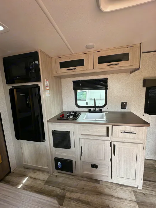 Inside an RV rental: a compact kitchen featuring a microwave, fridge, sink, stovetop, and ample light-toned cabinetry.. Crossroads RV Zinger Lite 2026
