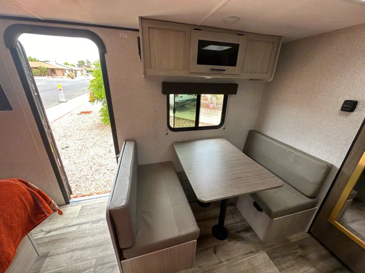 This inviting **rv rental** dinette features gray benches, a wood table, and overhead cabinets. An open door and window offer outdoor views.. Crossroads RV Zinger Lite 2026