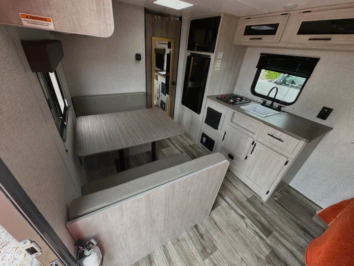 Bright RV rental interior featuring a cozy dinette, well-equipped kitchen with stove/sink, and wood-style flooring.. Crossroads RV Zinger Lite 2026