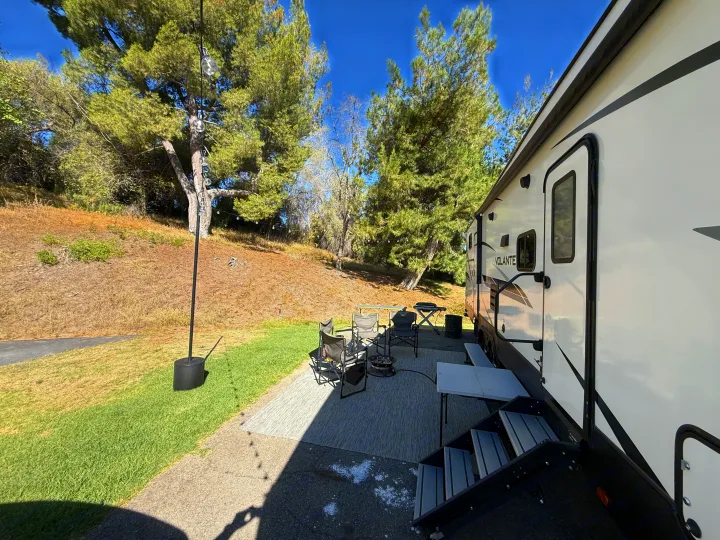 Perfect rv rental campsite featuring an RV, outdoor seating, fire pit, and tables under sunny trees.. Crossroads RV Volante 2022