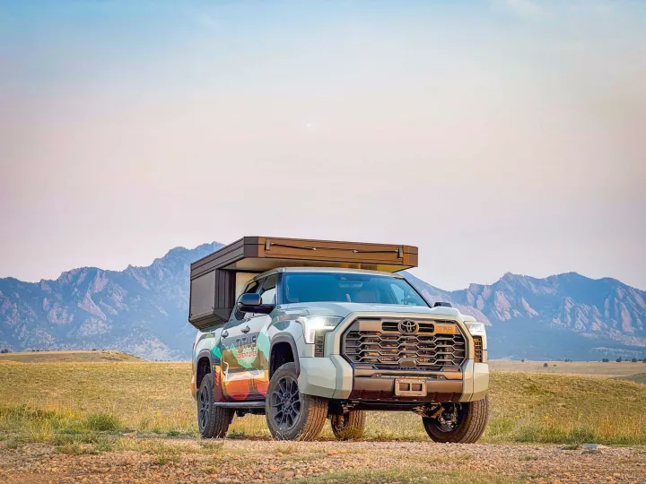 Adventure-ready Toyota Tundra RV rental with pop-up camper, parked off-road with scenic mountains in background.. Toyota Tundra 2026