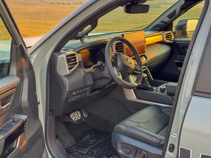 Modern truck interior with open door, showing driver's seat, steering wheel, and dashboard against a golden field. Perfect for an rv rental adventure.. Toyota Tundra 2026