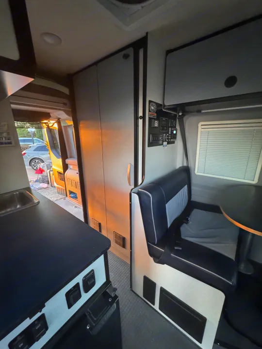 Inside an rv rental: a compact kitchen with sink, storage unit, and dinette area with seating and window blinds.. Winnebago Revel 2022