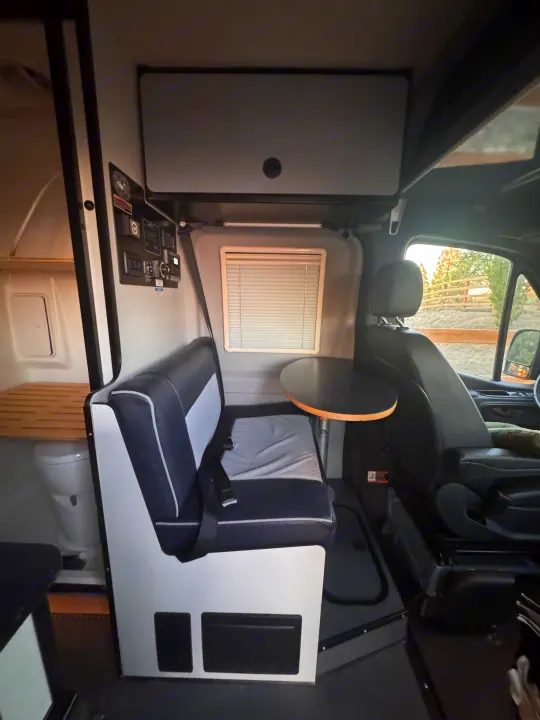 Interior of an RV rental, featuring a dining area with a bench seat and table, driver's seat, and a small toilet.. Winnebago Revel 2022