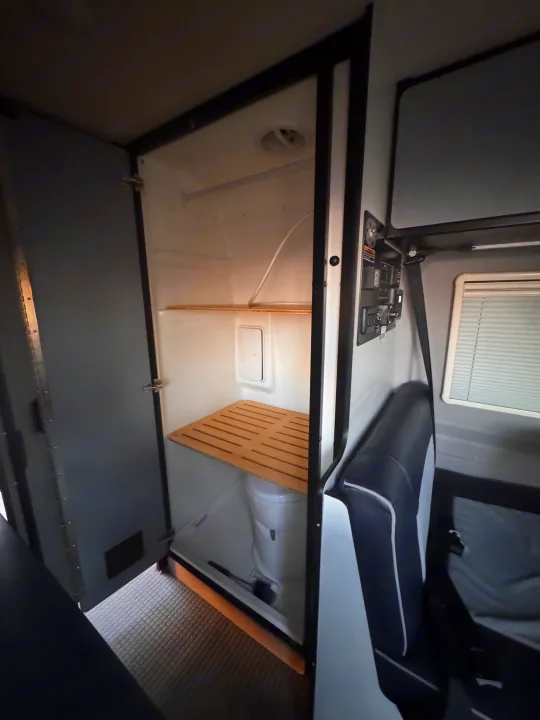 RV rental: view of a compact wet bath featuring a toilet, wooden slatted mat, and shower; alongside an RV seat and control panel.. Winnebago Revel 2022