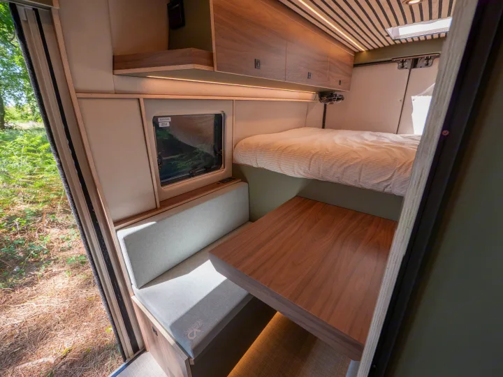Experience mobile living in this modern rv rental interior, featuring a raised bed, cozy dining nook, wood finishes, and integrated lighting.. Peugeot Boxer 2026