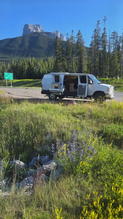 White RV rental van parked roadside with open doors; mountains, forest, & Three Sisters Blvd sign in view.. Ford Econoline 2011