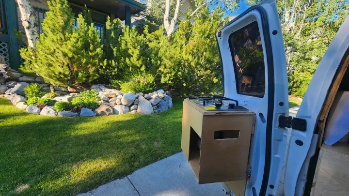 RV rental van with outdoor kitchen setup by a lush garden. Campervan cooking for van life adventures.. Ford Econoline 2011
