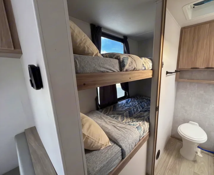 Two bunk beds with patterned bedding are seen next to a compact toilet area in this cozy **rv rental**.. Winnebago Access 2025