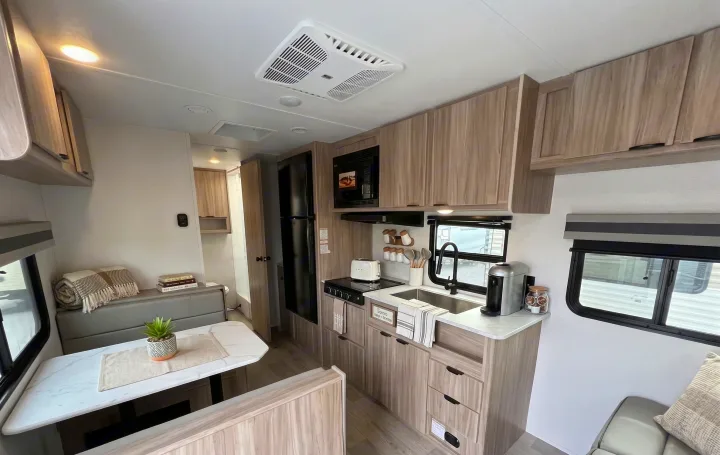 Modern RV rental interior, showcasing a full kitchen, dining nook, and cozy living area. Light wood and white decor throughout.. Winnebago Access 2025