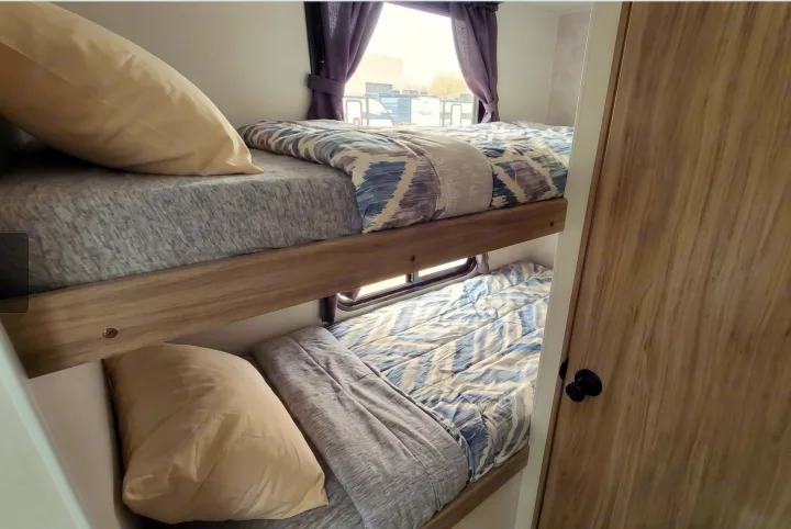 Inside this rv rental, cozy bunk beds offer a comfortable sleeping area with patterned bedding and a window for natural light.. Winnebago Access 2025