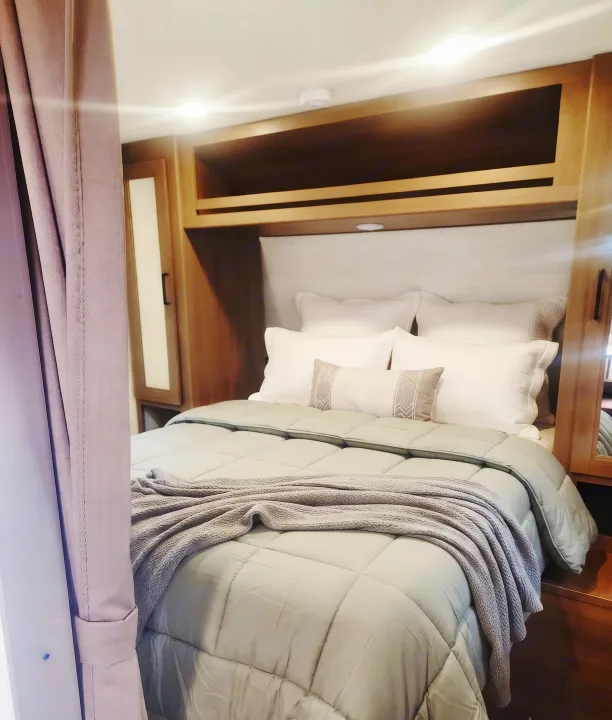 Cozy RV rental bedroom with soft bedding, wood cabinetry, and ambient lighting, perfect for a comfortable travel stay.. Grand Design Transcend Xplor 2025