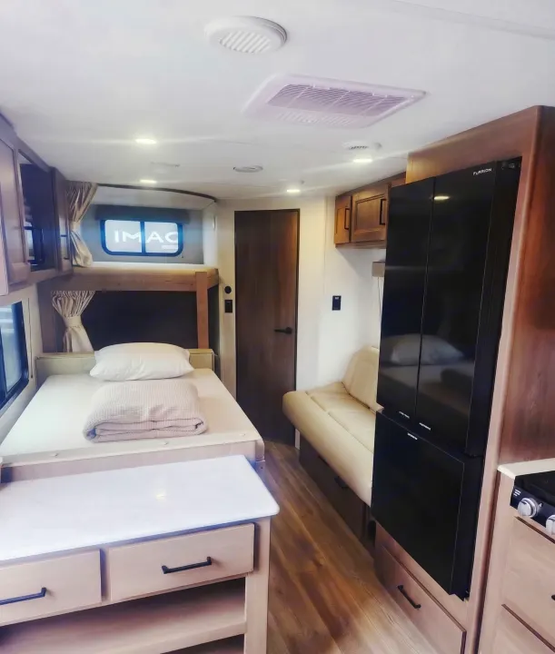 Spacious RV rental interior with bunk beds, kitchenette, sofa, and refrigerator, ideal for family adventures.. Grand Design Transcend Xplor 2025