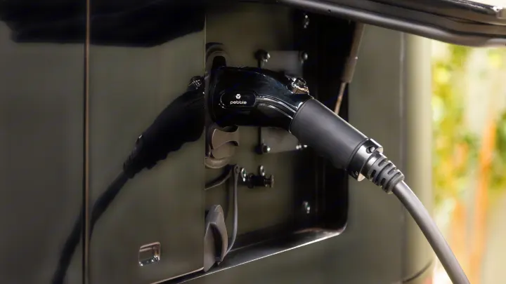 Close-up of a "Pebble" electric charging cable plugged into a dark RV's port. Power up your next electric rv rental adventure.. Pebble Flow 2026