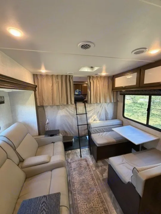Spacious RV rental interior: cozy living space with sofa, dining area with table, and ladder to an overhead bunk.. Gulf Stream Conquest 2023