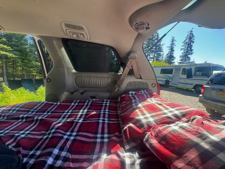 Cozy car camping bed (plaid) in SUV. View of an RV rental, trees, and sky from the open hatch. Perfect for a road trip!. Toyota Toyota Sienna XLE 2005