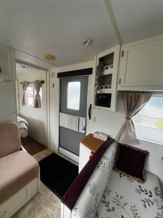 Cozy RV rental interior features a floral bench, cabinets, door, and a peek into the bedroom, offering a comfortable stay.. Kustom Koach Westwind 2004
