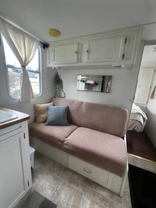 Cozy rv rental interior featuring a light-colored living space with a couch, small kitchenette, and a glimpse into the bedroom.. Kustom Koach Westwind 2004