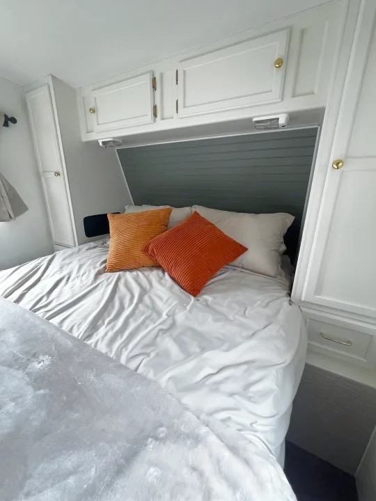 Cozy RV rental bedroom interior with gray bedding, vibrant orange pillows, and ample white built-in storage cabinets.. Kustom Koach Westwind 2004