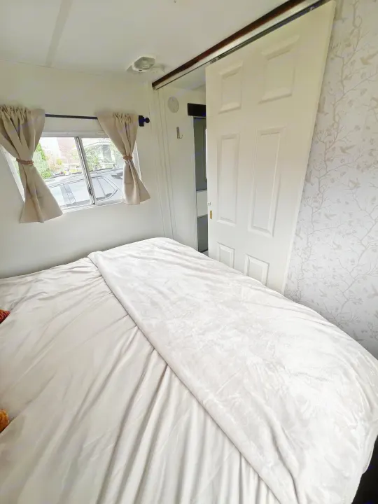 Cozy RV rental bedroom with soft bedding, window views, and a space-saving sliding door, offering a comfortable retreat.. Kustom Koach Westwind 2004