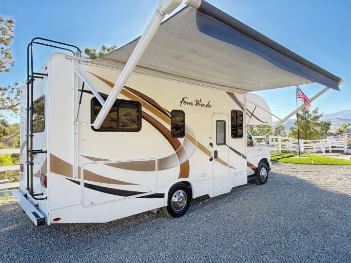 This Four Winds RV rental, with its extended awning, is parked on gravel, ready for scenic adventures.. Thor Four Winds 2019