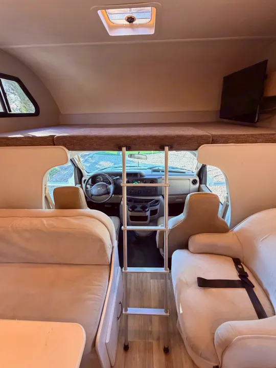 Interior of an rv rental, showcasing an overhead bunk, ladder to the front cabin, and comfortable dinette seating for travelers.. Thor Four Winds 2019