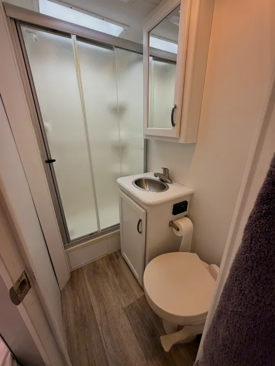Compact RV rental bathroom with shower, toilet, sink, mirrored cabinet, and small control panel on the vanity.. Thor Four Winds 2019