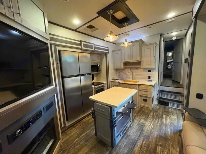 Modern RV rental interior: well-equipped kitchen with island & stainless steel appliances, plus a cozy living area with large TV.. Keystone Fuzion 2021