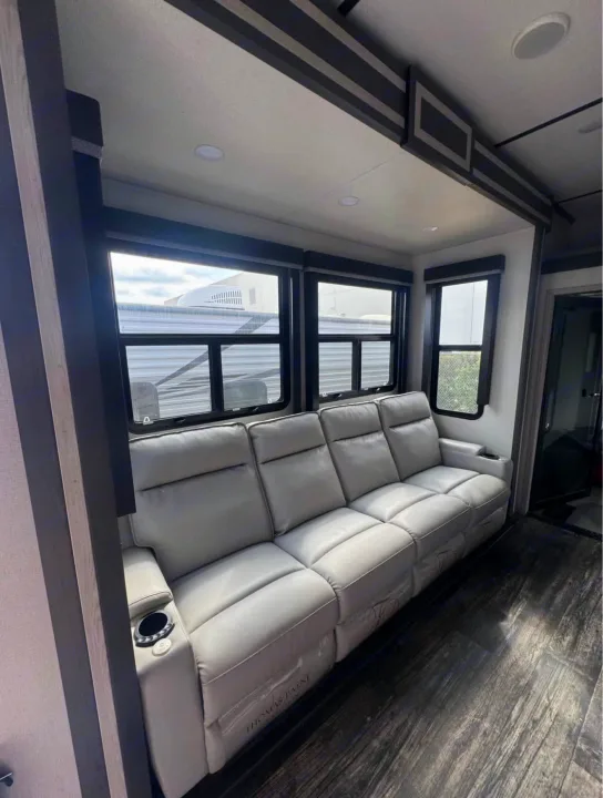 RV rental's inviting living area with a light gray reclining sofa, built-in cup holders, large windows, and dark wood-look floor.. Keystone Fuzion 2021