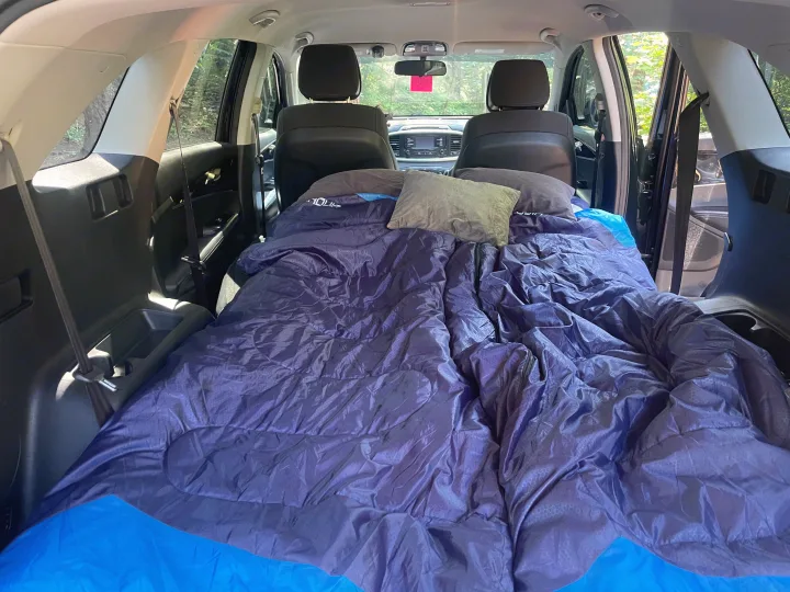 Inside an SUV, a blue sleeping bag & pillows make a comfy car camping setup, a versatile alternative to an rv rental for travel.. KIA Sorento 4X4 2017