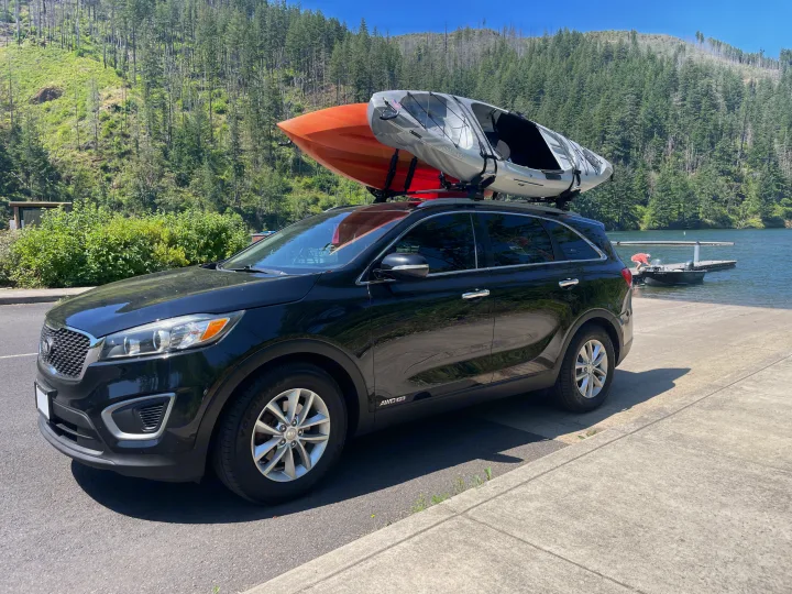 Black SUV with kayaks parked by a lake and forest for outdoor adventure. Plan your next trip, maybe with an RV rental!. KIA Sorento 4X4 2017