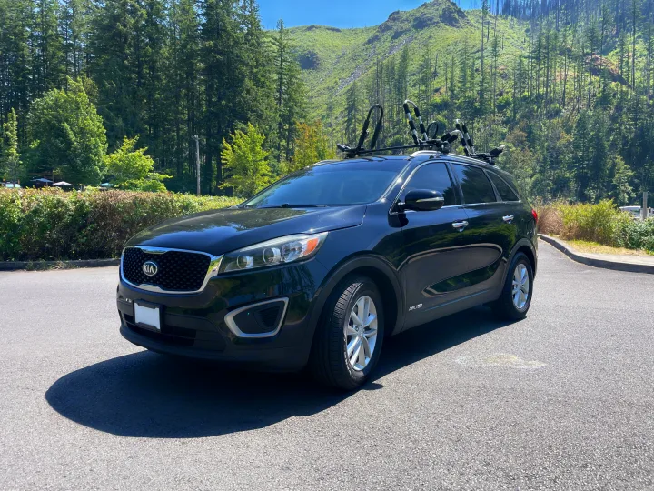 A black Kia Sorento SUV with kayak racks in a forest, ready for outdoor adventures, often booked alongside an rv rental.. KIA Sorento 4X4 2017