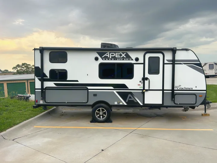 APEX Nano travel trailer, an rv rental, parked on concrete under cloudy skies. White, gray, and black exterior details.. Coachmen Apex Nano 2024