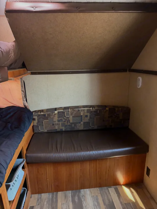 Cozy RV rental interior with a sleeping bunk and comfortable bench seat, featuring patterned backrests and under-bunk storage.. Starcraft Autumn Ridge 2015