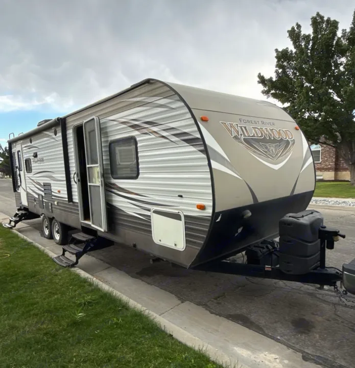 Wildwood travel trailer RV rental, parked and ready for adventure. A large RV with open door and steps on a cloudy day.. Forest River Wildwood 2017