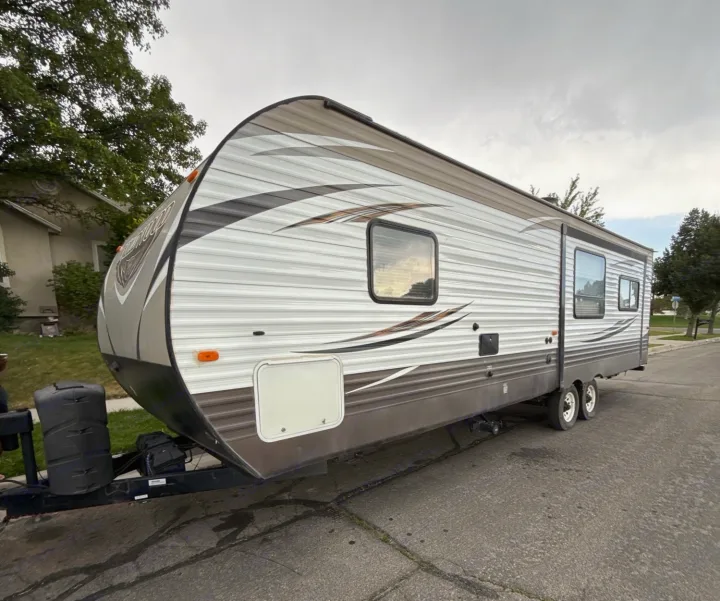 Spacious travel trailer RV rental, featuring a gray/white exterior and curved front, parked on a street for your next trip.. Forest River Wildwood 2017