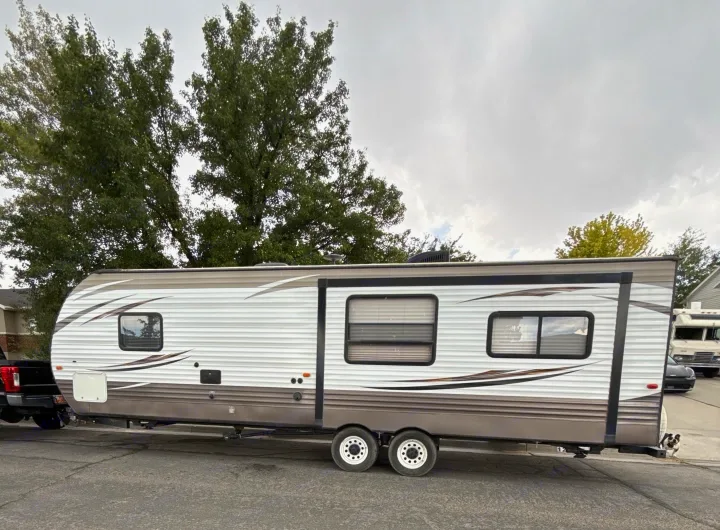 White & brown travel trailer (rv rental) with windows and a visible slide-out section. It's hitched to a truck; a small dog is by the rear.. Forest River Wildwood 2017