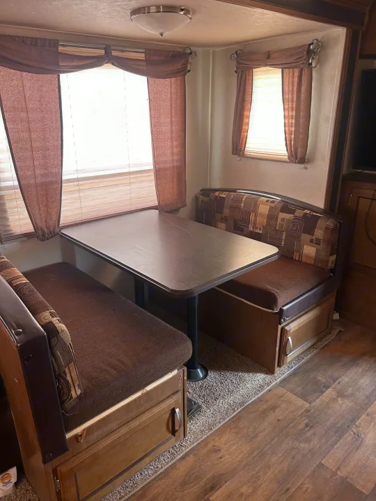 Cozy RV rental dinette featuring patterned bench seating, a table, and window treatments with storage beneath the benches.. Forest River Wildwood 2017