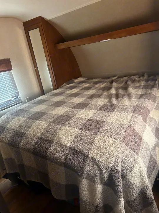Cozy RV rental bedroom featuring a bed with a gray and white checkered sherpa blanket, window, and wooden cabinetry.. Forest River Wildwood 2017