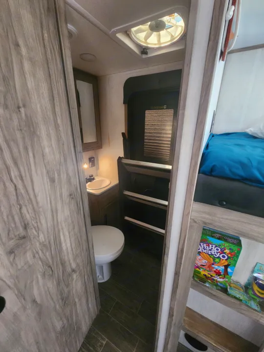 RV rental interior showing a compact bathroom with sink/toilet and bunk beds with a board game. Great for family trips!. Forest River Cherokee Alpha Wolf 2021