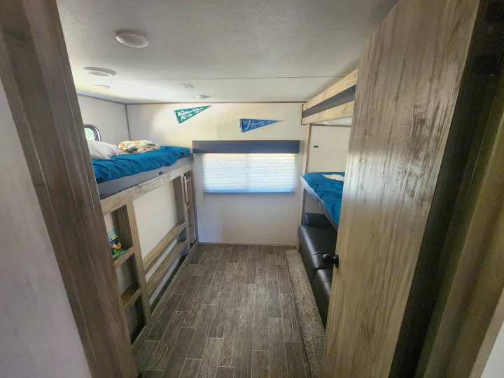Cozy RV rental interior with bunk beds, perfect for family adventures. The compact space features wood-look floors and wall decor.. Forest River Cherokee Alpha Wolf 2021