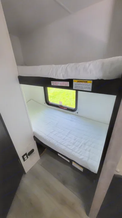 RV rental features comfortable bunk beds with a window overlooking green grass, ideal for family travel. Max load 275 lbs.. A Liner Ascape 2024