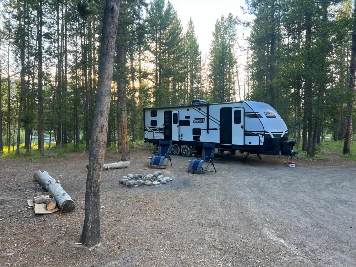 Ready for adventure! This spacious RV rental is perfectly set up at a serene forest campsite with a cozy fire pit and chairs.. Dutchmen Coleman Light 2022