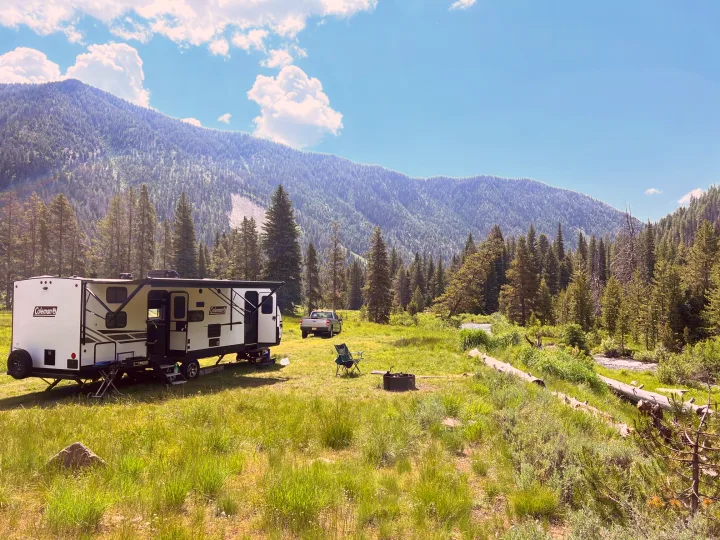 Scenic RV rental camping: travel trailer & truck by a river, nestled in a lush mountain valley forest.. Dutchmen Coleman Light 2022