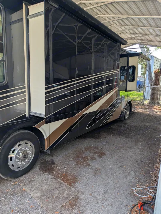 RV rental parked under a metal carport, its slide-outs extended. The glossy black side reflects the roof structure.. Forest River Berkshire 2018