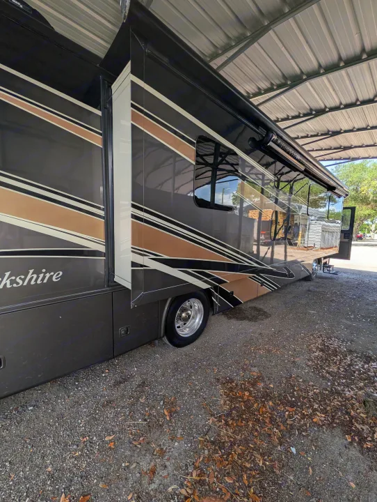 Large, sleek Berkshire RV rental with extended slide-out, parked under a corrugated metal shelter. Ideal for your next journey.. Forest River Berkshire 2018