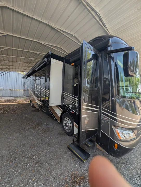 Black luxury RV rental under a carport with its door open and awning extended, ready for adventure.. Forest River Berkshire 2018