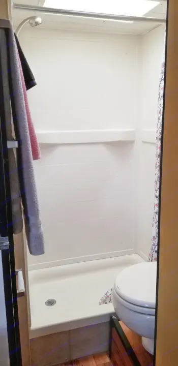 RV rental bathroom with a white shower, hanging towels, and a partial view of the toilet. A compact and functional space.. Thor Majestic 2013