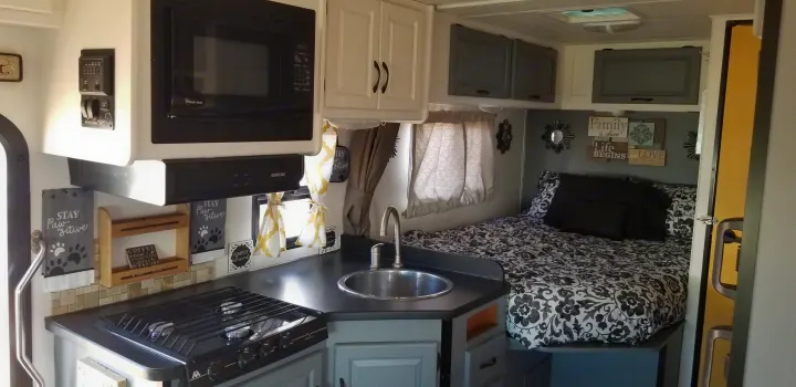 Cozy RV rental interior with a compact kitchen (microwave, stove, sink) and a comfortable bed, decorated in grey/white.. Thor Majestic 2013